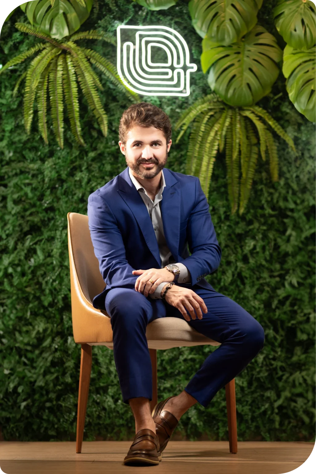 Dr. José Eduardo Araújo sentado na recepção da Clínica Integrative Care, diante da parede verde com o logotipo em neon.
